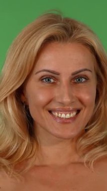 Çekici, olgun, dalgalı sarı saçları olan bir kadın ellerini şakaya vurarak yüzünü kapatıyor ve canlı, yeşil renkli bir arka plana karşı büyüleyici bir duygu yelpazesi sergiliyor. Bu anlamlı portre, izleyicileri duygularıyla bağlantı kurmaya davet ediyor.