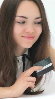 Uzun, dalgalı saçları olan neşeli genç bir kadın, bilgisayarına yakın bir yerde kredi kartını tutarak, kendinden emin bir şekilde satın alırken neşe saçıyor. Parlak, minimalist zemin, modern alışverişin özünü yakalayarak heyecanını arttırıyor.