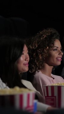 Canlı bir arkadaş ikilisi, biri parlak siyah saçlı ve diğeri güzel kıvırcık saçlı, komik bir filme dalmış, samimi bir sinemada kahkaha ve patlamış mısır paylaşıyorlar. Titreşimli atmosfer, en sevdiklerinin tadını çıkarırken heyecanla uğulduyor.
