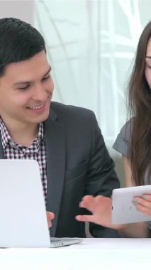 Dinamik genç bir iş adamı ve kadın, parlak ve modern bir ofis zeminine karşı hazırlanan parlak bir tablet üzerindeki verileri analiz ederken hareketli bir tartışmaya girişiyor. Odaklanmış ifadeleri ve enerjik enerjileri takım çalışması ve yenilik ruhunu somutlaştırıyor.