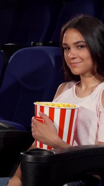 Neşeli genç bir kadın, lüks bir sinema koltuğunda otururken klasik çizgili patlamış mısır kovasını tutarak neşeyle ışıldıyor. Bu canlı sahne film gecelerinin heyecanını özetliyor, izleyicileri filmin büyüsüne dalmaya ve kahkahalarımızı paylaşmaya davet ediyor.