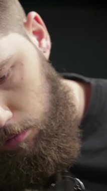 Çarpıcı sakallı ve titizlikle odaklanan uzman bir berber şık, modern bir berber dükkanında erkek bir müşteri için şık bir saç kesimi ve sakal kesimi yapıyor. Enerjik atmosfer yaratıcılıkla uğulduyor, tımar sanatının ve