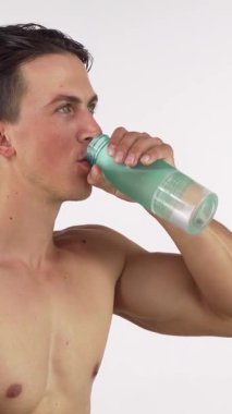 Formda ve güzel vücutlu yakışıklı bir adam canlandırıcı bir egzersizden sonra serin bir içecekle kendini ferahlatırken ışıl ışıl gülümser. Bu dinamik sahne sağlık ve zindelik yayar, kendini adamış bir yerde susuzluğun temel rolünü vurgular.