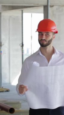 Canlı turuncu şapkalı genç, sakallı bir inşaat mühendisi inşaat halindeki binayı inceliyor, elinde kendine güvenen bir gülümsemeyle ayrıntılı planlar tutuyor. Ham beton ve iskele ile çevrelenmiş, yenilik ruhunu somutlaştırıyor ve