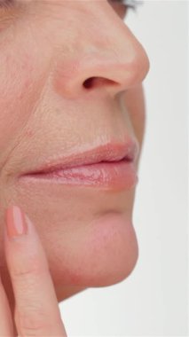 A captivating close-up of a graceful middle-aged woman gently caressing her flawless skin against a pristine white backdrop. Her luminous complexion and tranquil expression radiate beauty and self-care, emphasizing the significance of skincare at