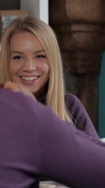 Büyüleyici bir kafede, neşeli bir kadın erkek arkadaşına şakacı bir şekilde dilini uzatıyor, elinde sahneye biraz sıcaklık katan beyaz bir bardak tutuyor. Onun ışıl ışıl gülüşü ve sıradan mor süveteri davetkar bir atmosfer yaratırken, erkek arkadaşı...