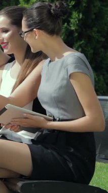 Three stylish young women exude joy and confidence as they celebrate a successful business contract outdoors, surrounded by lush greenery. Their vibrant outfits and animated expressions create a dynamic atmosphere of teamwork and ambition, reflecting