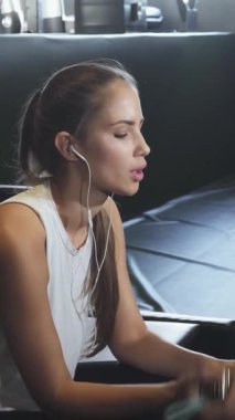 A fit young woman in trendy sportswear takes a revitalizing sip from her aqua-colored water bottle, pausing to recharge after an intense gym session. The sleek gym backdrop, adorned with modern equipment and soft ambient lighting, amplifies her