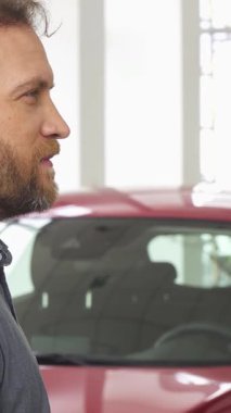 A delighted, bearded man radiates happiness as he holds up his sleek car keys in front of a dazzling red automobile. This vibrant scene encapsulates the thrill of new ownership, highlighting the joy and pride of purchasing a vehicle in a modern, well