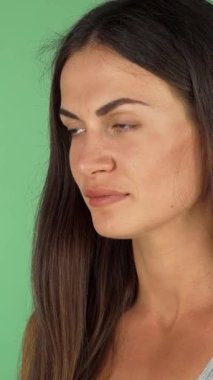 A beautiful young woman with flowing brunette hair enjoys a refreshing sip from a tall glass of crystal-clear water, exuding joy and vitality. Against a vibrant green chromakey backdrop, her confident smile and serene expression embody the essence of