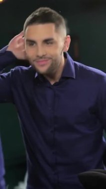 A young man with a meticulously groomed beard thoughtfully examines his reflection in a vintage barber shop mirror, embodying the essence of modern masculinity. The vibrant atmosphere, adorned with chic decor and professional grooming tools, elevates