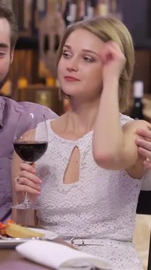 A delightful couple, radiating joy, clinks their elegant wine glasses filled with deep red wine in a cozy restaurant. The intimate setting, illuminated by soft, warm lighting and adorned with tasteful decor, creates a magical atmosphere as they