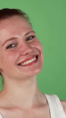 This vibrant studio portrait showcases a joyful woman with striking red hair, radiating positivity as she confidently displays an OK sign against a lively green chromakey backdrop. Her infectious smile and playful spirit create an inviting