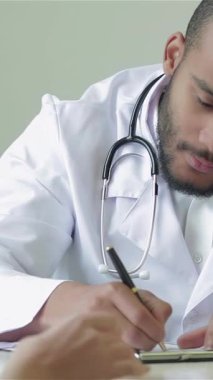 In a bright, modern clinic, a dedicated doctor with a warm smile attentively writes a prescription while engaging with his patient. The inviting atmosphere radiates trust and professionalism, showcasing the caring bond between the multi-ethnic doctor