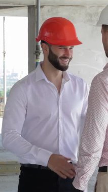 A young architect in a crisp white shirt and a builder wearing a bright orange hard hat share a firm handshake amidst the vibrant chaos of a construction site. This dynamic moment of collaboration showcases the synergy between design and construction