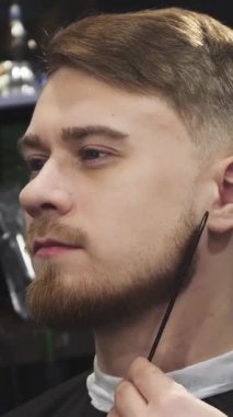 A close-up of a stylish young man with a meticulously groomed beard, beaming as a skilled barber deftly trims his facial hair with precision clippers. This intimate scene radiates self-care and masculinity, highlighting the artistry of grooming in a