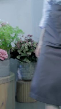 An attractive Caucasian female florist gracefully squats near a vase, skillfully rearranging stunning bouquets of white flowers amidst a delightful array of colorful blooms. Surrounded by rustic decor and the sweet scent of nature, she embodies