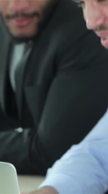 In a contemporary office space, two determined businessmen passionately discuss strategic objectives while analyzing vibrant reports and charts displayed on a sleek laptop. Their sharp formal attire and intense focus radiate professionalism and