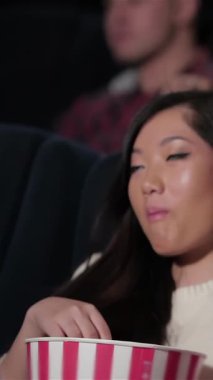 Two joyful girlfriends share infectious laughter and popcorn, fully immersed in their movie night adventure. The cozy theater buzzes with excitement, illuminated by the screens glow, as vibrant popcorn buckets add a playful touch to their delightful