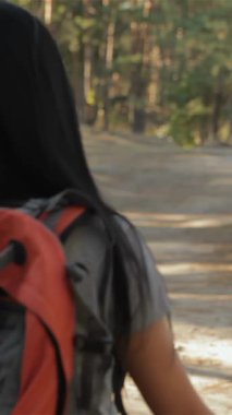 A charming couple embarks on a romantic hike, hand in hand, basking in the warm sunlight filtering through the lush green trees. The brunette woman glances back with a radiant smile, her long hair flowing gracefully, while the bearded man shares a