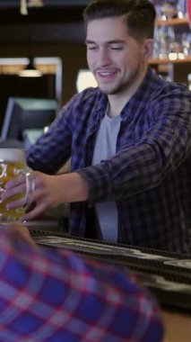Three cheerful friends gather at the pub counter, raising frosty mugs of beer in a toast while sharing laughter and engaging in lively conversation. The warm, inviting atmosphere, accentuated by the bartenders friendly service and vibrant decor