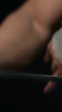 A close-up of a muscular man expertly wrapping a training belt around his hands, emphasizing his sculpted biceps and powerful physique. The striking black background amplifies the intensity of his workout preparation, evoking a sense of determination