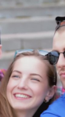 Three vibrant friends, glowing with happiness, strike a playful pose on outdoor steps, snapping a fun selfie. Their radiant smiles and trendy sunglasses embody the essence of a carefree summer day, filled with laughter and unforgettable memories