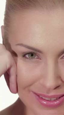 This captivating portrait features a beautiful Caucasian woman with flawless, glowing skin, gently caressing her face against a pristine white backdrop. Her serene expression and soft glow radiate confidence and purity, highlighting her natural