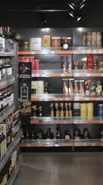 Genç bir çift hipermarketin hareketli alkol reyonunda geziniyor, tramvayları taze ürünlerle dolup taşıyor. Sakallı adam bir şişeyi entrikayla incelerken kız arkadaşı da ona doğru eğilip paylaşılan keyifli bir an yaratıyor.