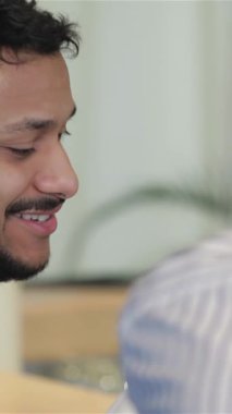 Two cheerful friends engage in a spirited conversation, their laughter resonating in a cozy bar filled with warm lighting. One man, with a stylish beard and a radiant smile, leans in animatedly, celebrating the joy of friendship over drinks in a