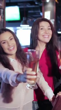 A vibrant scene unfolds as four old friends, two men and two women, exuberantly toast with frosty glasses of beer at a lively bar. Their radiant smiles and cheers echo the excitement of camaraderie, as they celebrate friendship and the thrill of the