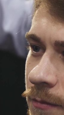 This captivating close-up features a young man with striking blue eyes, lost in thought as a skilled barber meticulously shapes his hairstyle. The vibrant barbershop ambiance enhances the artistry of grooming, showcasing a blend of tradition and