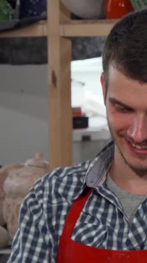 A lively scene showcases a young, handsome male potter, radiating joy as he expertly shapes clay into a stunning bowl. His vibrant studio, filled with colorful ceramic pieces and artistic tools, exudes creativity and warmth, inviting viewers into his
