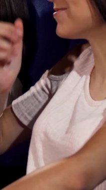 A vibrant scene captures three young women bursting with laughter, sharing popcorn, and reveling in the joy of a comedy film at the cinema. Their glowing smiles and animated expressions create an inviting atmosphere, perfect for a weekend filled with