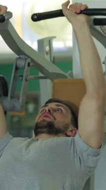 A focused young man of Middle Eastern descent is intensely engaged in chest muscle exercises, lifting weights with unwavering determination. The gyms vibrant atmosphere, filled with bright colors and dynamic energy, highlights his muscular physique