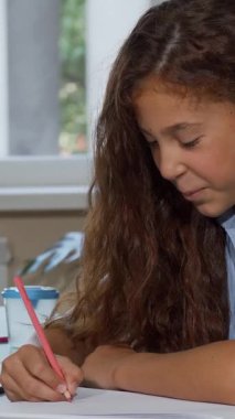 A joyful long-haired girl is fully immersed in her drawing at school, her radiant smile lighting up the room as she engages with her art. Surrounded by a vibrant array of colorful art supplies, this enchanting scene captures the essence of creativity