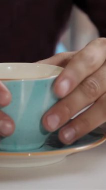 A close-up showcases a pair of male hands tenderly lifting a delightful blue coffee cup from its elegant saucer. This inviting scene exudes warmth and comfort, beckoning coffee enthusiasts to indulge in the rich aroma and exquisite flavor of their
