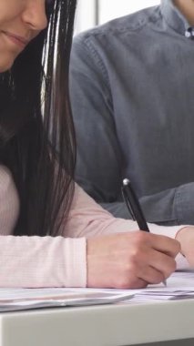 A close-up shot features a woman in a chic pink top, confidently signing documents while a professional salesman stands beside her at a vibrant car dealership. This dynamic scene captures the thrill of purchasing a new vehicle, emphasizing the