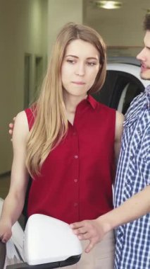 A charming young couple stands closely together, eagerly examining a sleek convertible at the dealership, their faces glowing with excitement and affection. The handsome man, in a casual checkered shirt, gently rests his hand on his beautiful