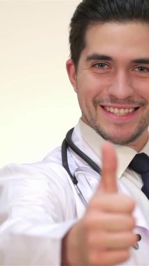 A confident young male doctor in a pristine white coat flashes a thumbs-up, exuding positivity and professionalism. With a stethoscope elegantly draped around his neck and a warm, inviting smile, he embodies the essence of healthcare, inspiring trust