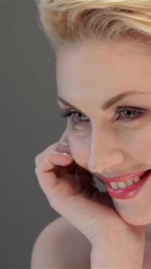 An elegant woman with luminous skin and captivating green eyes smiles gently, her graceful pose enhancing the soft gray backdrop. This stunning portrait captures her natural beauty and confidence, inviting admiration and warmth