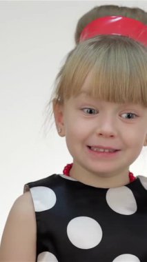 A delightful young girl in a playful polka-dot dress and striking red arm warmers expresses pure astonishment, her hands covering her mouth in disbelief. Her sparkling blue eyes and joyful smile radiate a whimsical charm, inviting viewers into her