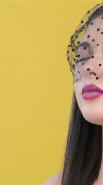 A breathtaking Asian woman, elegantly draped in a delicate black veil, closes her enchanting eyes while inhaling deeply against a vibrant yellow backdrop. This captivating portrait exudes sophistication and sensuality, highlighting her flawless skin