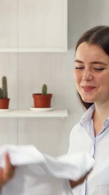 In a vibrant workshop brimming with creativity, two young female fashion designers passionately discuss their latest clothing collection while showcasing a stylish white garment. Surrounded by colorful fabrics and chic designs, their collaboration