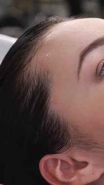 A close-up view showcases a beauticians expert hands gently massaging shampoo into the scalp of a delighted young woman, radiating bliss in a stylish spa setting. The serene ambiance, combined with the soothing sound of flowing water, creates a
