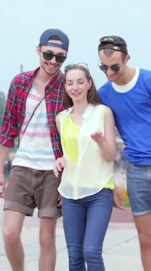 Three stylish young friends stroll down a lively street, exchanging laughter and vibrant stories under a radiant blue sky. Their carefree energy and trendy outfits illuminate the scene, embodying the spirit of summer adventures and cherished