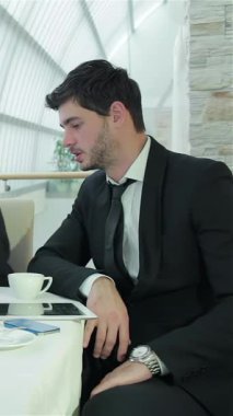 A sharply dressed man in a sleek black suit is deeply immersed in a collaborative business meeting, showcasing a blend of professionalism and concentration. The modern office setting, with its elegant decor and natural light, enhances the atmosphere