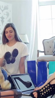 Three vibrant friends, filled with excitement, sit on a cozy floor, eagerly trying on chic shoes surrounded by colorful shopping bags. Their laughter echoes as they share fashion tips and capture playful selfies on a laptop, creating a lively