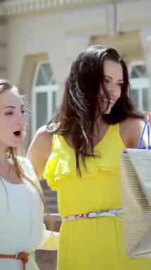 Three fashionable girls, each holding vibrant shopping bags, exude pure joy as they stroll down the sunlit street, their laughter harmonizing with the lively urban atmosphere. The warm sunlight dances on their stylish outfits, highlighting their