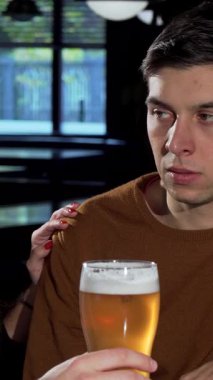 In a cozy pub, a young man sits pensively at the bar, while his friends surround him, offering drinks and laughter to lift his spirits. This vibrant scene beautifully illustrates the warmth of friendship, highlighting the uplifting power of